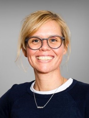 Portrait von Kathrin Kerschbaumer. Sie hat blonde Haare, trägt eine Brille und lächelt.